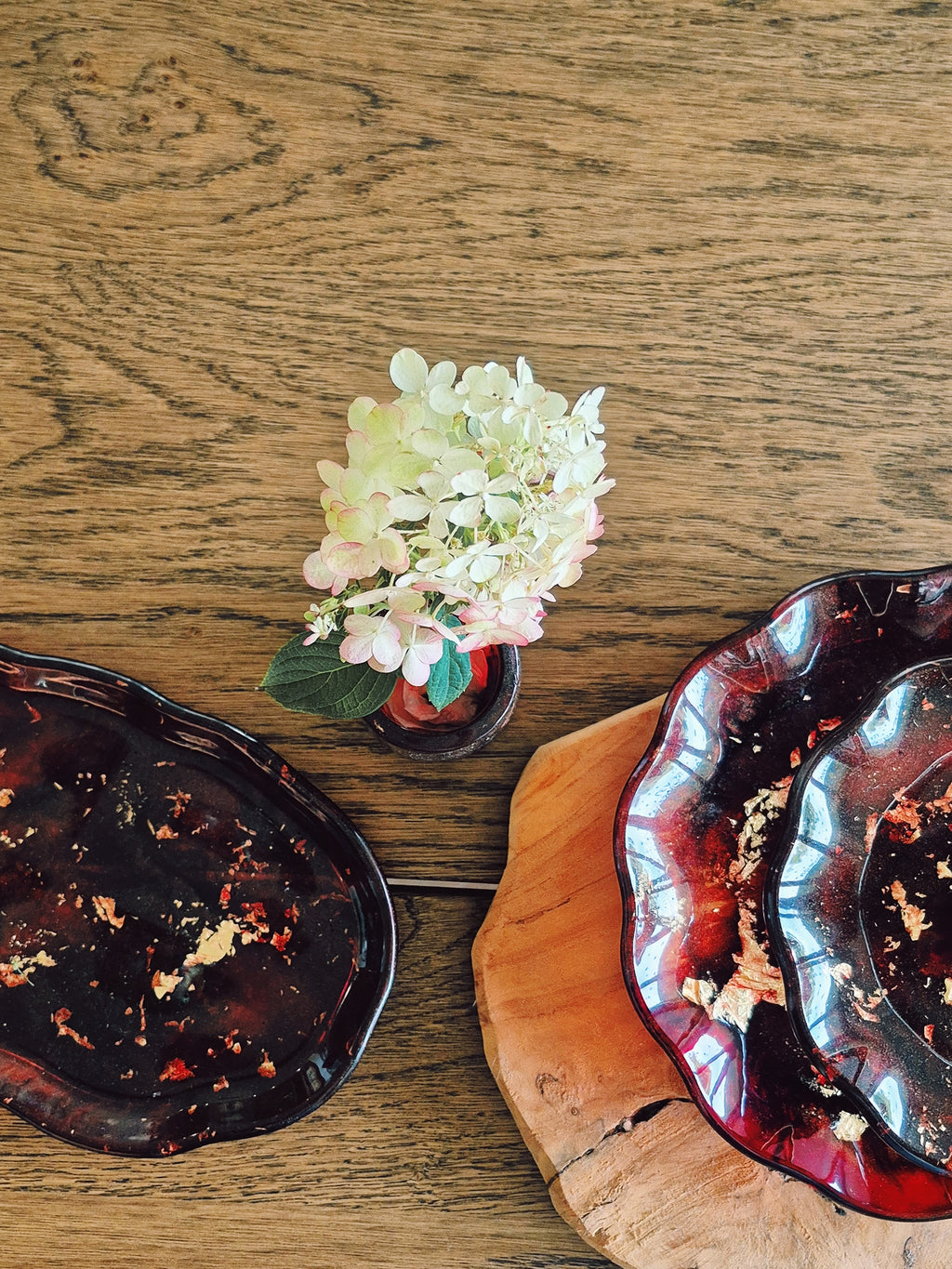 Teller und Etagere aus Epoxidharz in Rot-Gold, dekorativ auf Holzplatte mit Blüte platziert – Kollektion Falling Ember