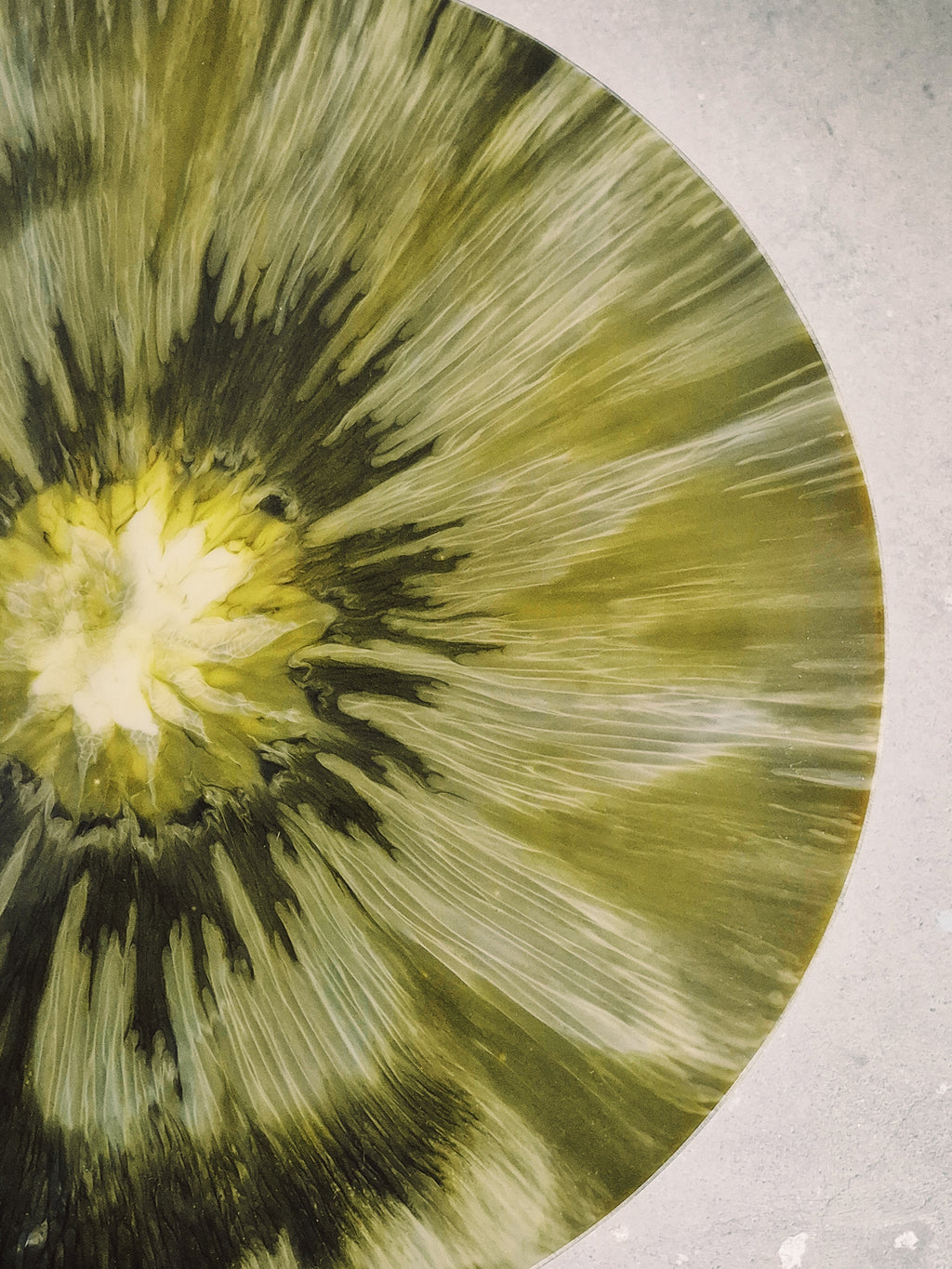 Nahaufnahme der Tischoberfläche des Beistelltischs „Green Ember“ mit leuchtendem goldgrünem Zentrum und strahlenförmiger, marmorierter Struktur in Epoxidharz.