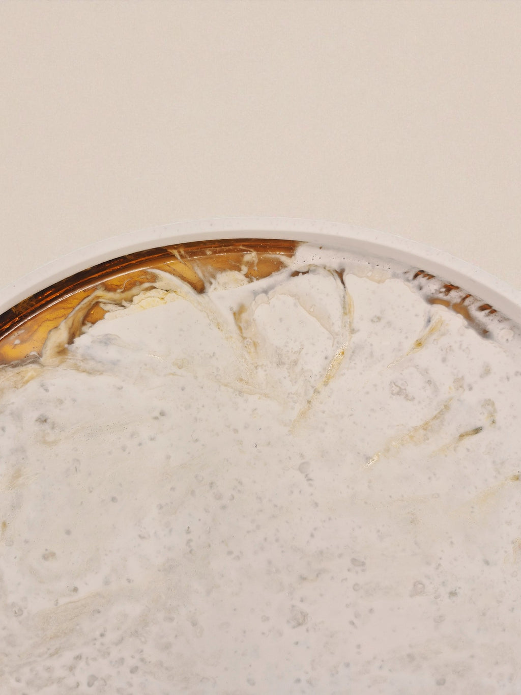 Draufsicht auf rundes Tablett „Melted Sun“ in Gold und Weiß, glänzende Oberfläche mit fließendem Übergang zwischen Harz und Jesmonite.