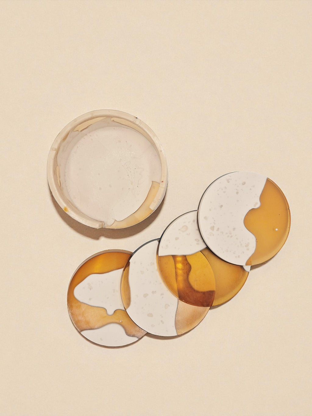 Draufsicht auf das Untersetzer-Set „Melted Sun“ mit cremefarbenen und goldtransparenten Flächen, auf beigem Hintergrund fotografiert.