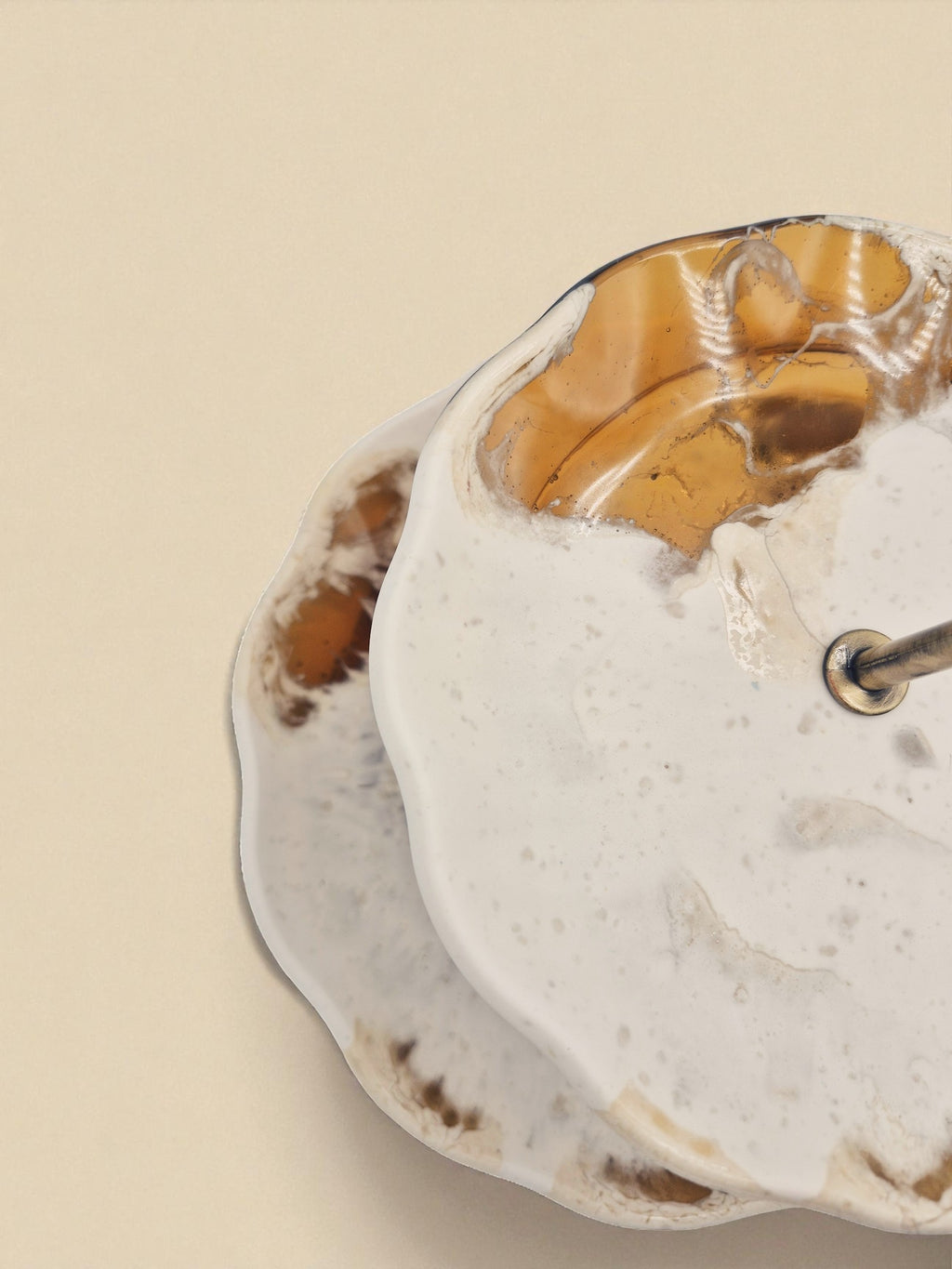 Nahaufnahme der oberen Etage der Etagere „Melted Sun“ mit fließendem Muster in Creme und Bernsteinfarben auf beigem Hintergrund.