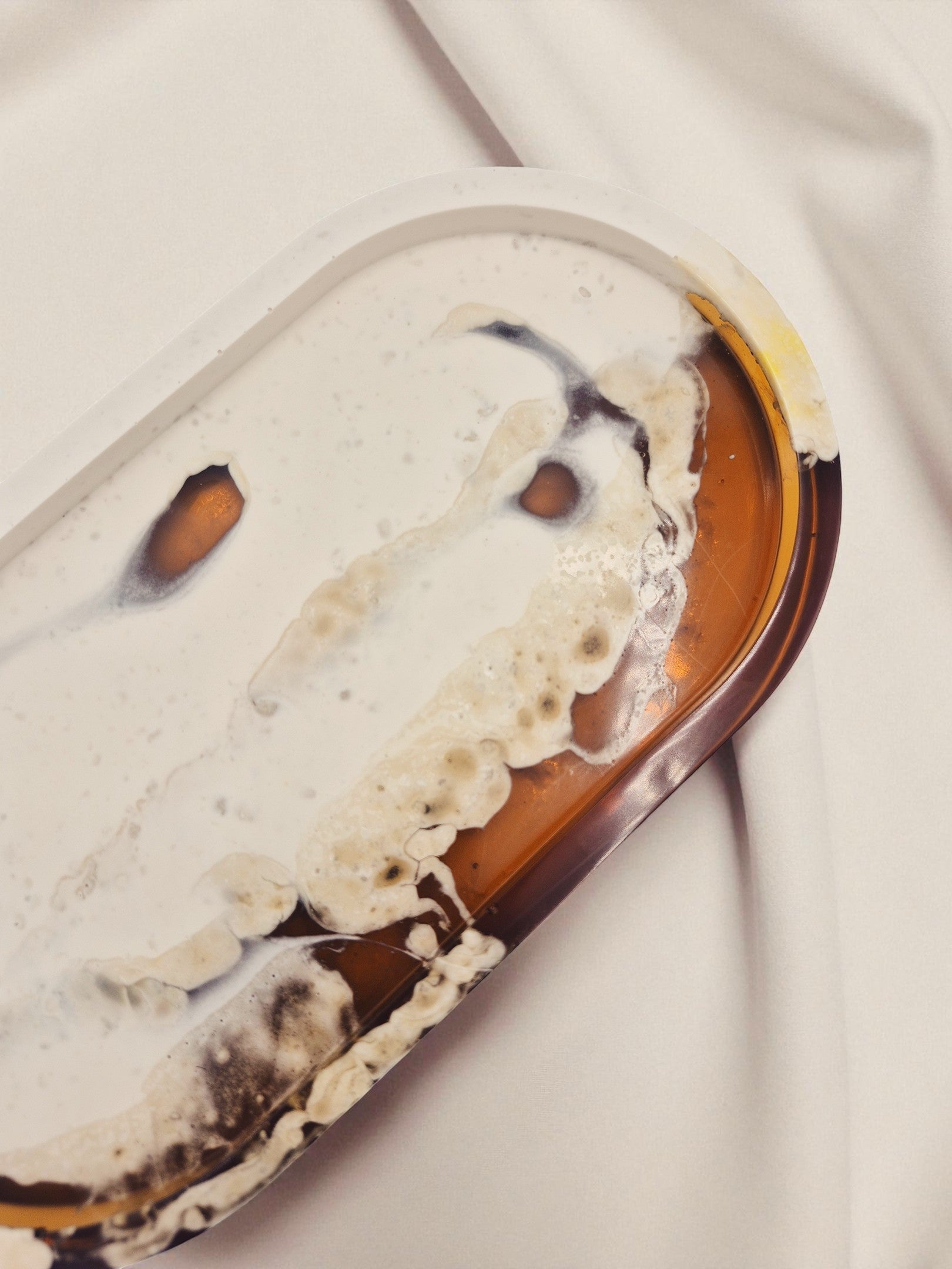 Tablett „Melted Sun“ in ovaler Form aus Jesmonite und Epoxidharz, dekorativ vor beigem Stoff im warmen Licht platziert.